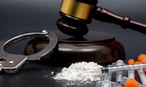Drug crime concept with handcuffs, gavel, white substance, and syringes.
