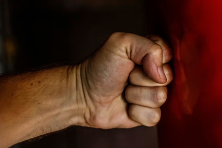 A close-up of a clenched fist raised near a surface, shown against a dark background.